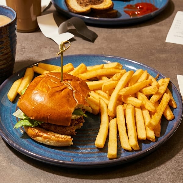 A partially eaten burger and fries on a blue plate, with a coffee mug and drink nearby.